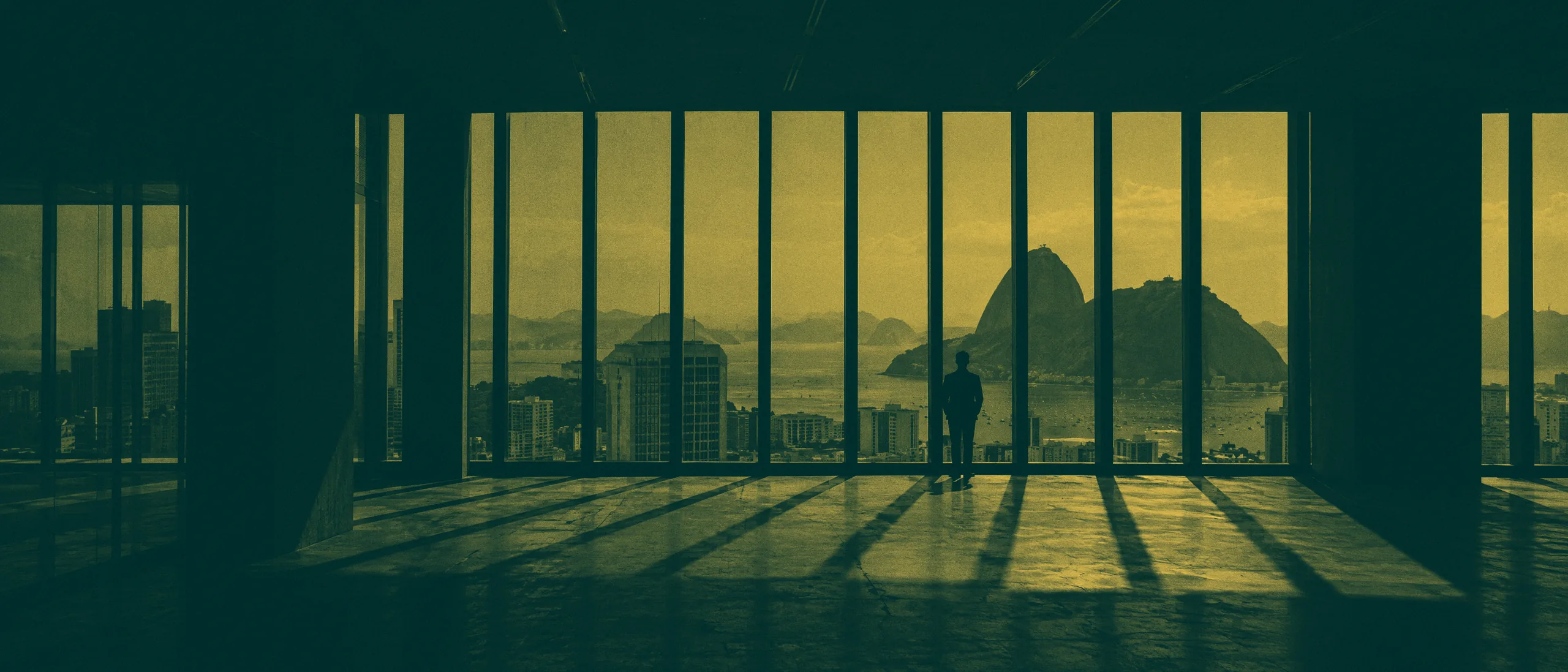 Pessoa vista de costas junto a uma janela alta, ao fundo de um escritório