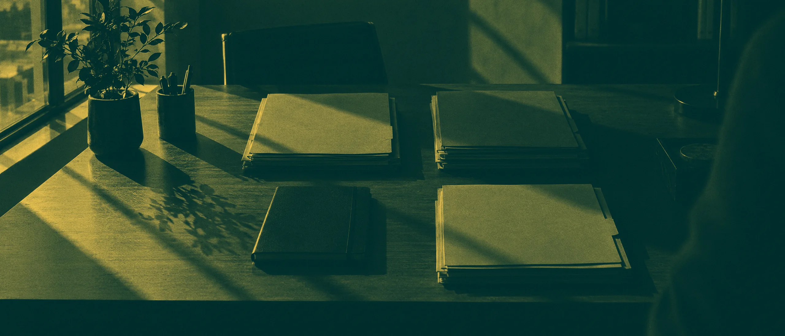 Mesa de trabalho com pastas e caderno organizados sob luz de janela
